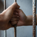 A pair of hands holding prison bars